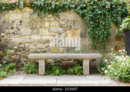 Banco in un giardino formale con un vecchio muro di pietra Foto Stock