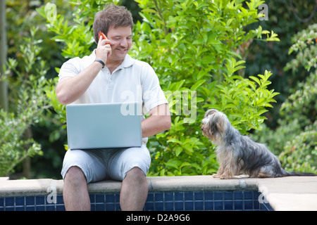 L'uomo mediante telefono cellulare e computer portatile all'aperto Foto Stock