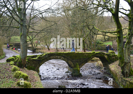 Donna che cammina su Packhorse bridge spanning Wycoller Beck in inverno nella frazione di Wycoller Foto Stock