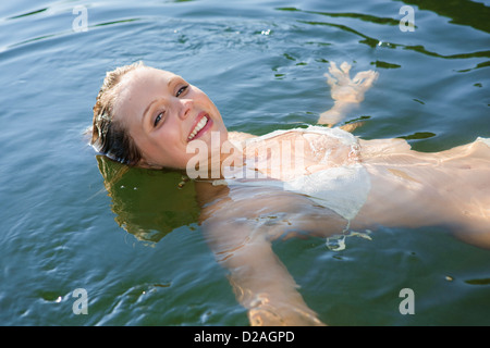 Donna sorridente galleggianti nel lago ancora Foto Stock