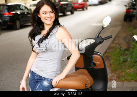 Donna appoggiato su di uno scooter su strada di città Foto Stock