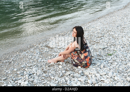 Donna seduta sulla spiaggia rocciosa Foto Stock