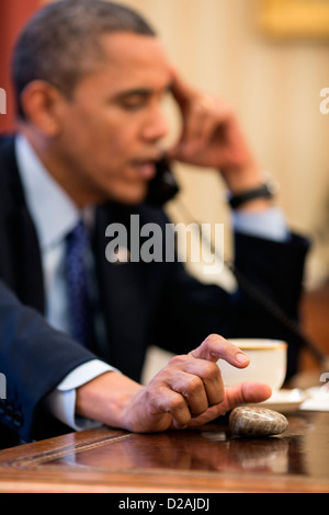 Il presidente statunitense Barack Obama gioca con una pietra di Petoskey come egli parla al telefono in ufficio Ovale della Casa Bianca il 6 dicembre 2012 a Washington, DC. Una pietra di Petoskey è di fossili di corallo dal Michigan inferiore della penisola. Foto Stock