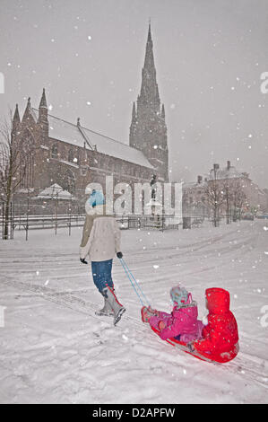 Giovane madre Joanne Grumett traina una slitta con i suoi due giovani ragazze per godere la neve in condizioni di blizzard in Piazza del Mercato, Lichfield, Staffordshire, Regno Unito. Venerdì 18 Gennaio 2013. St Mary's Center e Boswells statua e Dr Johnsons's House in background. Foto Stock