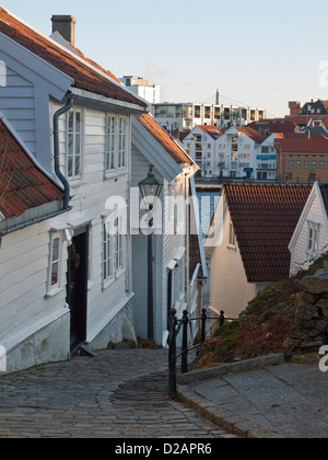 Ripida strada di ciottoli e case di legno in vecchio Stavanger Norvegia .Harbour può essere visto qui sotto Foto Stock