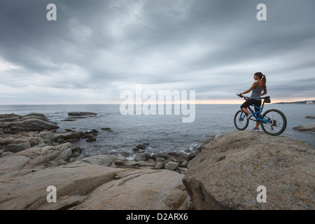 Donna in piedi con la bicicletta sul boulder Foto Stock