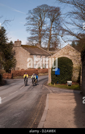 3 ciclisti maschio insieme sulla bici, angolo di arrotondamento & Escursioni in bicicletta lungo la strada di campagna in scenic villaggio rurale - Bolton Abbey, North Yorkshire, Inghilterra, Regno Unito. Foto Stock