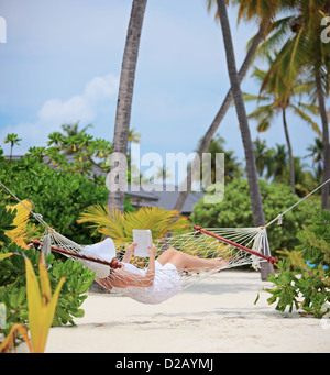 Donna rilassante in un amaca e la lettura di un libro su una spiaggia delle Maldive, girato con una inclinazione e spostamento lente Foto Stock