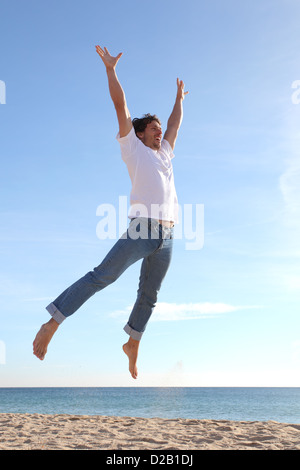 L'uomo jumping happy in spiaggia con un cielo blu in background Foto Stock