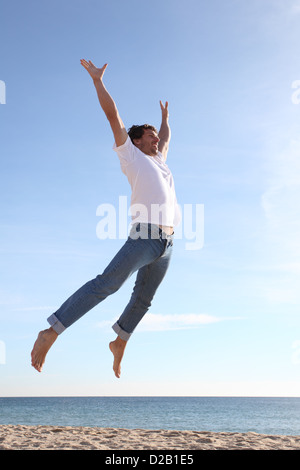 L'uomo jumping happy in spiaggia con un cielo blu in background Foto Stock