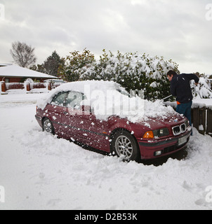 Un uomo con una scopa a spazzola neve profonda fuori la sua auto nel vialetto. Foto Stock