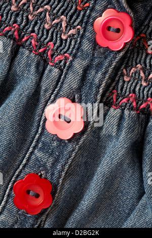 pulsanti a forma di fiori rossi e rosa a margherita e soffocante abito smok in denim per bambina Foto Stock