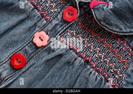 pulsanti a forma di fiori rossi e rosa a margherita e soffocante abito smok in denim per bambina Foto Stock