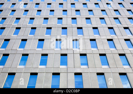 Calcestruzzo facciata di edificio per uffici con modello regolare delle finestre che riflettono il cielo blu Foto Stock