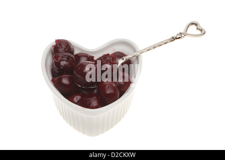 Conserve di amarene in un cuore ramekin sagomato con un cucchiaio isolata contro bianco Foto Stock