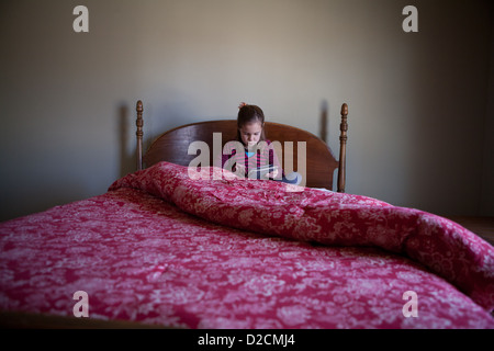 7 anno vecchia ragazza si siede sul letto utilizzando un ipad. Foto Stock