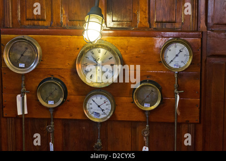 Gli indicatori di antiquariato e un orologio montato su un pannellate di legno paratia a bordo di una barca. Foto Stock