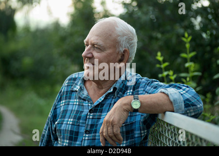 Un anziano uomo appoggiato su di una recinzione e guardando lontano serenamente Foto Stock