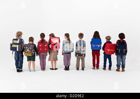 Un gruppo di bambini della scuola di zaini da indossare e che si trova in piedi in una fila, vista posteriore Foto Stock