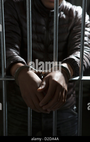 Un prigioniero dietro le sbarre con mani ammanettato Foto Stock