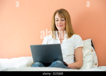 Donna di mezza età utilizzando un computer portatile per navigare in internet mentre giacente sul suo letto. Foto Stock