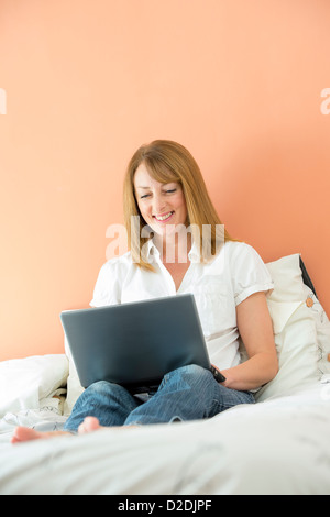 Donna di mezza età utilizzando un computer portatile per navigare in internet mentre giacente sul suo letto. Foto Stock