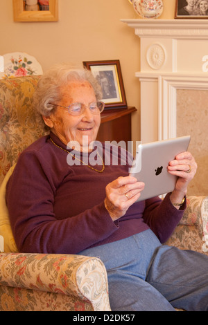 Donna anziana pensionata con gli occhiali su ipad apple tablet a casa rilassarsi sulla sedia la riproduzione di giochi per computer Foto Stock