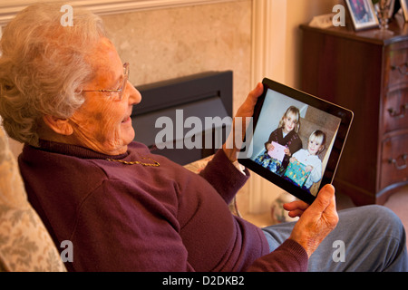 Donna anziana pensionata con gli occhiali su ipad apple tablet a casa rilassarsi sulla sedia guardando fotografia dei nipoti Foto Stock