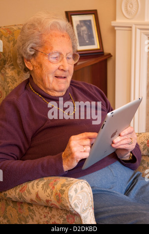 Donna anziana pensionata con gli occhiali su ipad apple tablet a casa rilassarsi sulla sedia la riproduzione di giochi per computer Foto Stock