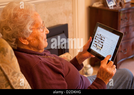 Donna anziana pensionata con gli occhiali su ipad apple tablet a casa rilassarsi e fare un cruciverba giornale on-line Foto Stock