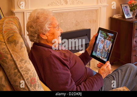 Donna anziana pensionata con gli occhiali su ipad apple tablet a casa rilassarsi sulla sedia guardando le fotografie dei nipoti Foto Stock