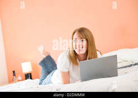 Donna di mezza età utilizzando un computer portatile per navigare in internet mentre giacente sul suo letto. Foto Stock