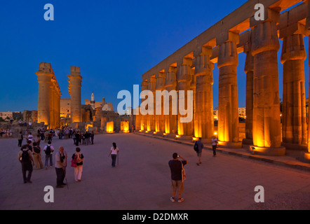 I turisti a passeggio tra le colonne illuminati della corte di Amenhotep III Tempio di Luxor al tramonto Luxor Egitto Medio Oriente Foto Stock