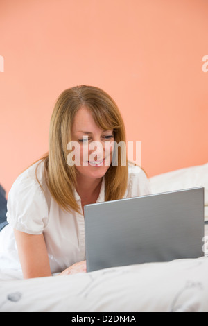 Donna di mezza età utilizzando un computer portatile per navigare in internet mentre giacente sul suo letto. Foto Stock
