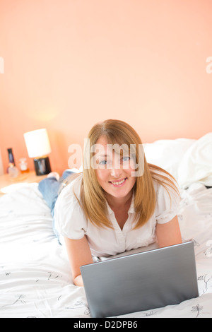 Donna di mezza età utilizzando un computer portatile per navigare in internet mentre giacente sul suo letto. Foto Stock