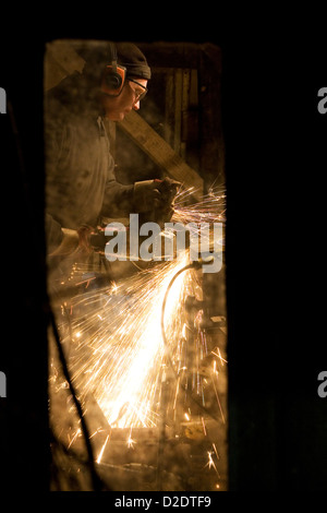 Immagine di un uomo preso attraverso una finestra di lui usando il disco elettrico mola di taglio creando un sacco di scintille da red hot metal. Foto Stock