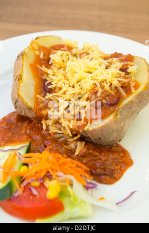 Jacket potato essendo servita con peperoncino e formaggio grattugiato. Foto Stock