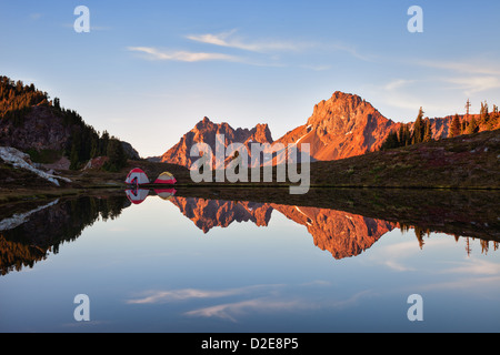 Le cime frastagliate in Sunset Glow e riflessa in Tarn con escursionista e tende Foto Stock