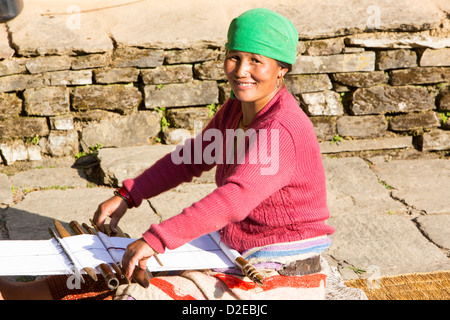 Una donna nepalese in abbigliamento tradizionale tessitura su un telaio a mano nei foothills dell'Himalaya, Nepal. Foto Stock