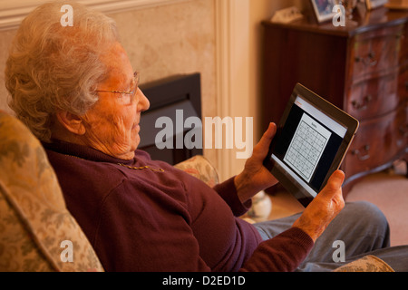 Donna anziana pensionata con gli occhiali su ipad apple tablet a casa rilassarsi sulla sedia gioca a Sudoku game Foto Stock