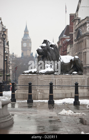 Lion statua in Trafalgar Square su un nevoso, inverno mattina con il Big Ben in background, London, England, Regno Unito Foto Stock