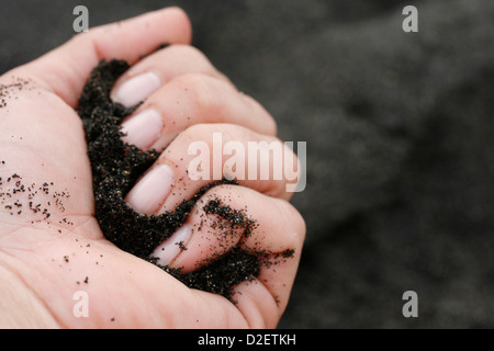 Una donna di mano trattiene una manciata di sabbia nera vulcanica da una delle spiagge di Tenerife (Isole Canarie). Foto Stock