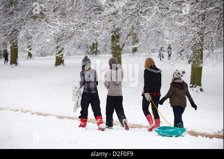 4 ragazze tirando una slitta attraverso la neve sulla loro strada in salita Foto Stock