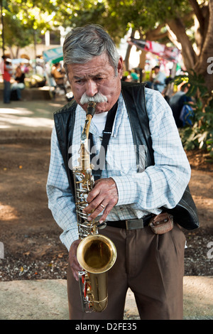 Il vecchio uomo musicista di strada attore con folte baffi bianchi intensamente svolge il suo sassofono in Zocalo Oaxaca de Juarez Mexico Foto Stock