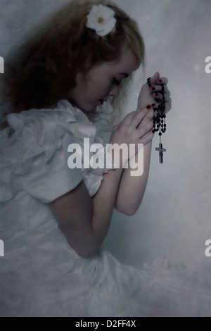 Una ragazza in un abito bianco è pregare con un rosario Foto Stock