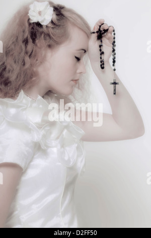 Una ragazza in un abito bianco è pregare con un rosario Foto Stock