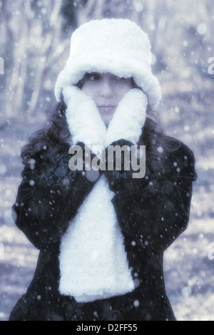 Una donna con un mantello nero, bianco guanti, sciarpa e cappello al di fuori durante la nevicata Foto Stock