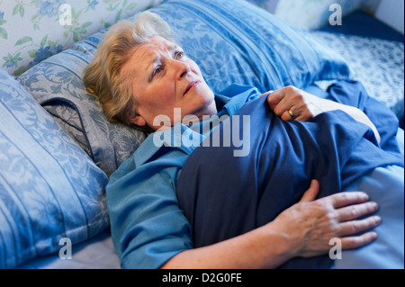 I vecchi pensionati donna giaceva a letto guardando preoccupato / sconvolto Foto Stock