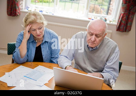 Coppia matura utilizzando un computer portatile, preoccuparsi per le loro bollette e debiti online Foto Stock