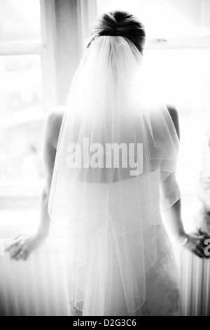 Foto in bianco e nero di una sposa guardando fuori della finestra con la schiena e il velo rivolto verso la telecamera Foto Stock